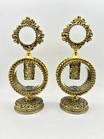 Front view of pair of vintage perfume bottles showing round clear glass bodies encased in ornate gold-tone filigree metal with decorative bases and stoppers.