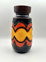 Front view showcasing the vase's colors and textured wave pattern in orange, yellow, and black on a cylindrical body with a brown neck and base.
