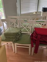 Overview of eight white wooden chairs with stacked green and red cushions