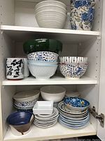 Cabinet shelf with various bowls, small plates, and mugs in different colors and patterns.