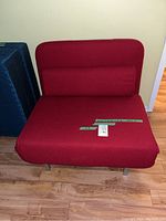 Front view of red convertible chair bed folded up with cylindrical bolster pillow, metal legs