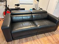 Front view of black leather sofa with headrests lowered, showing seat cushions and armrests