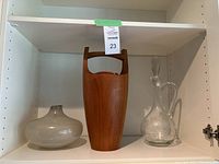 Shelf with three items: a squat round speckled gray glass vase, a tall wooden Dansk teak ice bucket with handle, and a tall clear glass decanter with stopper.