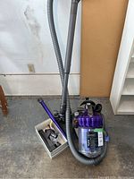 Dyson DC23 vacuum cleaner with hose and base unit placed on garage floor alongside box of attachments.