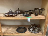 Shelf row with assorted electroplated copper serveware including lidded trays, warming stand, and tea service.