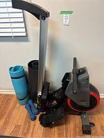 Folding rowing machine with exercise accessories including blue yoga mat and blue dumbbells.