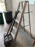 Full view of folded aluminum step ladder and two snow shovels leaning against it