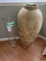 Photo of both vases together showing relative sizes and forms; glass vase approximately 28 inches tall and clear, contrasting with large gold painted vase with wide rounded shape.
