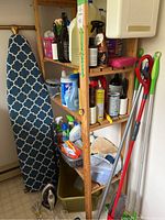 Full view of shelving unit with laundry supplies, ironing board, and cleaning tools.
