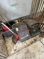 Photo showing Black & Decker electric lawnmower, electric weed eater, and grey bin with spray bottles and garden items on a tiled outdoor floor.