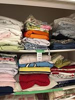 Shelves stacked with folded assorted linens including bed sheets, towels, quilts, and tablecloths in various colors and patterns.