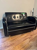 Front view of black faux leather loveseat with white piping on wood floor