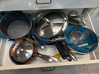 Top drawer opened showing assortment of pots and pans with protectors, including lids, colander, bowl, and measuring cups.
