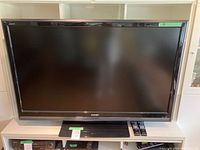 Front view of Sharp Aquos 52-inch flat-screen TV placed on a white TV stand with a soundbar below the screen.