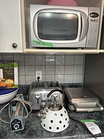 Overall photo showing Panasonic microwave on shelf, stainless steel toaster, teapot and Thermos pie maker on countertop with blue sealer machine.