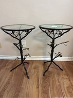 Two small matching end tables with metal frame and glass tops. Metal branches and bird decor are visible on bases.