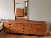 Front view of nine-drawer teak dresser with attached mirror reflecting background.