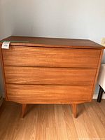 Front view of three-drawer teak dresser showing overall design and tapered legs