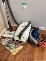 Kenmore Elegance canister vacuum and Dirt Devil portable vacuum placed on hardwood floor with various vacuum bags and attachments beside them.