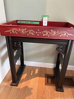 Full view of the red painted wooden tray sitting on a dark wooden stand with carved details on the legs and supports.