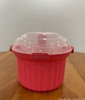 Pink cupcake carrier container with clear dome lid closed, shown on wooden table.