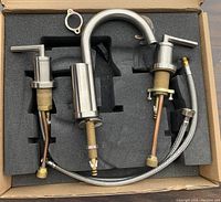 View of the faucet set showing the spout and two lever handles laid out in foam inside the box.