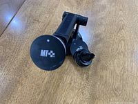 Close-up image of the MT+ logo on circular end of the phone holder arm next to the clip attachment.