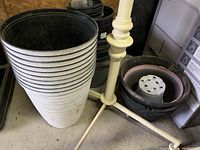 Stack of tall white plastic planters beside black planters and a white plant stand