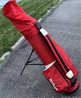 Red Wilson golf stand bag with padded strap and zippered storage pocket, setup outdoors on asphalt near grass