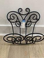 Front view of the black wrought iron garden hose hanger showing ornamental scrollwork and retail tag.