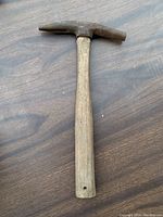 Pick hammer with wooden handle and pointed metal head lying on wooden surface