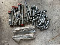 Photo showing a loose pile of shiny metal bolts with red caps, expansion bolts with metal sleeves and plastic rings, and some washers in plastic bags on a concrete floor.