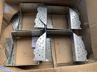 Box containing 8 galvanized steel heavy duty joist hangers arranged flat showing their shape and hole pattern.