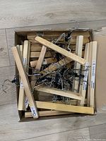 Top view of a box filled with natural finish wooden pants hangers from Ikea, showing multiple hangers overlapping with visible metal hooks and clips.