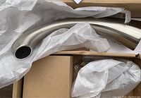Photo showing curved brushed nickel faucet spout wrapped in protective material inside box