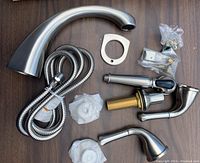 Bathtub fixture components laid out showing spout, hand shower, hose, and mounting hardware on a wooden surface.