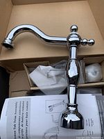 Photo showing the curved chrome faucet spout with polished finish and accompanying plumbing set in a box.