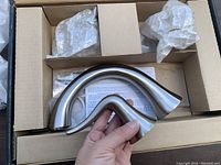 Boxed Luxury Taju bathroom fixture parts with curved brushed nickel faucet pieces and plumbing hardware visible.