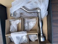 Photo of several brushed nickel plumbing parts packed in a box with protective wrapping showing spout and handles.