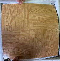 Close up of a single peel and stick vinyl floor tile showing wood grain panelled pattern in light oak shades.