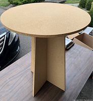 Small round side table made from cork, showing round flat surface and intersecting cross base supports made of cork panels.