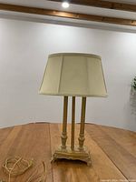 Front view of fabric barrel shade table lamp with dusty gold finish base on wooden surface.
