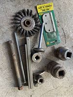 Overview of tools and hardware lot showing wire cup brush, door hinge package, threaded rod, square bar and socket wrench heads on concrete floor.