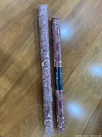 Two rolls of wallpaper on wooden floor. Shows both rolls with visible rolled pattern and wrapping.