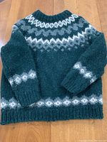 Front view of a green hand-knitted wool sweater showing the full pattern and knit texture.