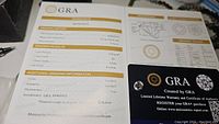 Photo showing GRA grading report with details of the moissanite stone including 2.0 carat weight, D color, VVS1 clarity, round brilliant cut, 8.0 mm size and excellent cut grade.
