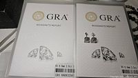 Two GRA moissanite report folios side by side with earrings placed on right report
