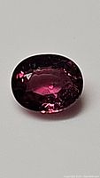 Close up photo of oval cut purple pink sapphire gemstone showing rich coloration and facets.