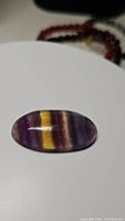 Oval deep color fluorite gemstone with purple, yellow, and striped color bands.