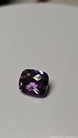 Close-up image of a single purple amethyst gemstone with cushion cut and checkerboard faceting, showing deep purple color and clarity.